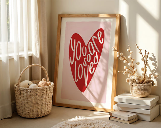 Kids wall art with white border, pink background, red heart and the words ‘you are so loved’ in white hand written text.