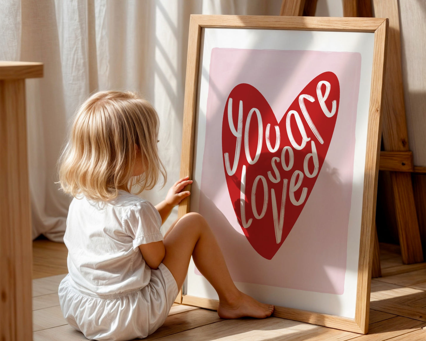 Kids wall art with white border, pink background, red heart and the words ‘you are so loved’ in white hand written text.