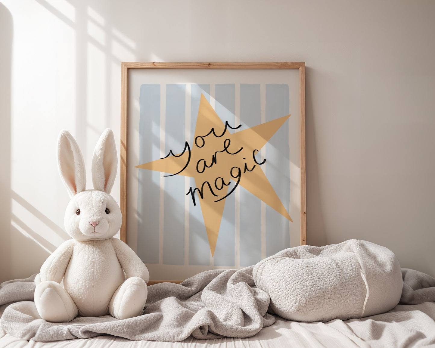 Framed artwork with a yellow star and 'You are magic' text on a light blue background, leaning against a white wall.