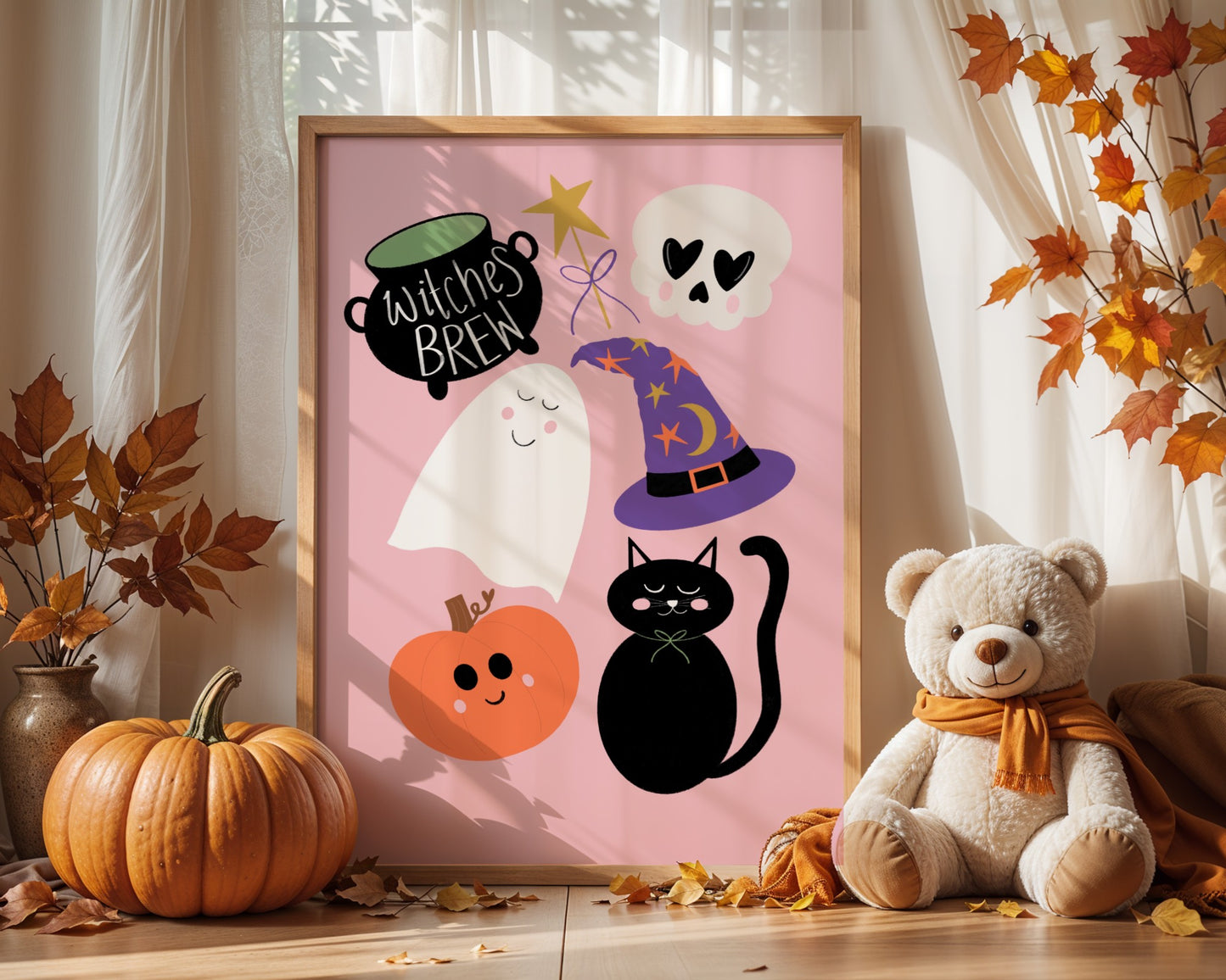 Framed Halloween-themed artwork with ghosts, a cat, a pumpkin, and a witch's brew pot on a pink background. Teddy bear and pumpkins in the foreground.
