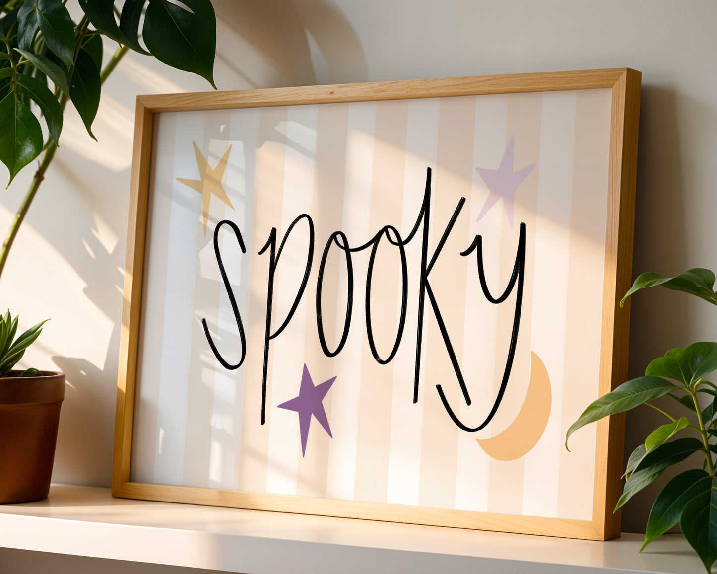 Framed artwork with the word 'Spooky' on a shelf with plants.