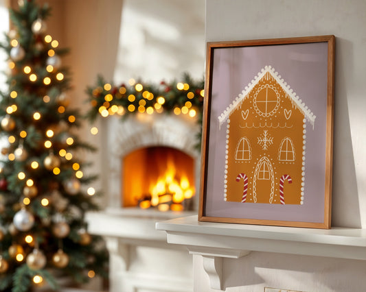 Framed gingerbread house artwork on a mantelpiece with a Christmas tree and fireplace in the background.