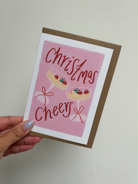 Hand holding a Christmas card with pink background and festive design.