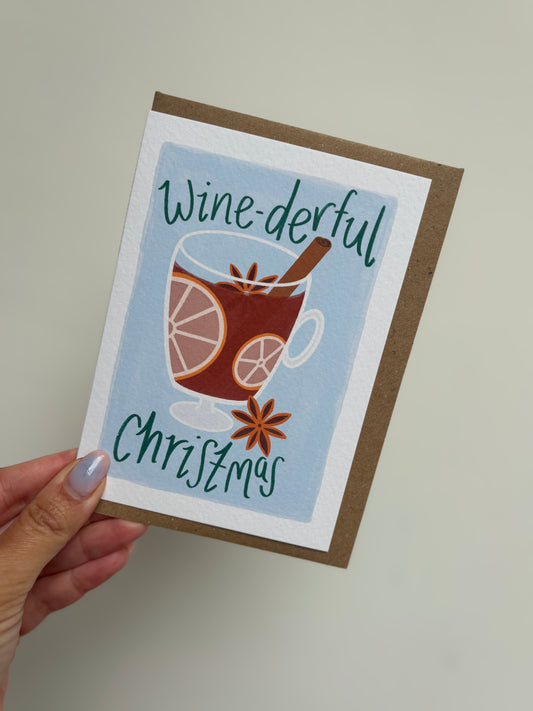 Card with a glass of mulled wine and text 'Wine-derful Christmas' held by a hand.