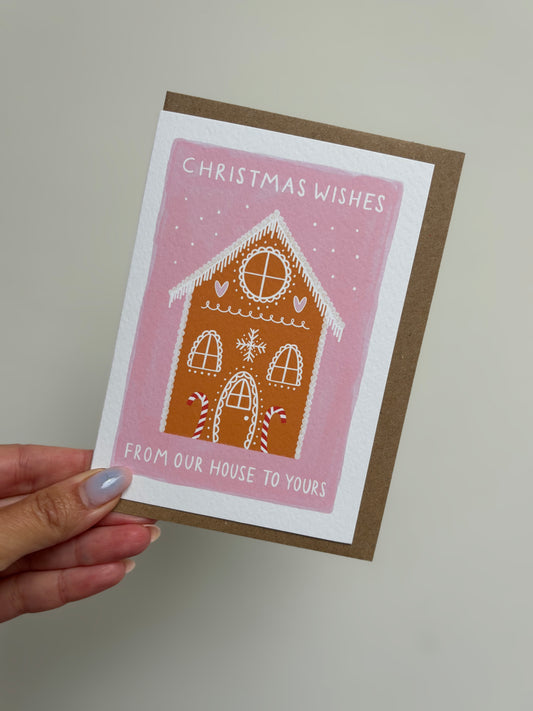 Hand holding a Christmas card with a gingerbread house design on a plain background