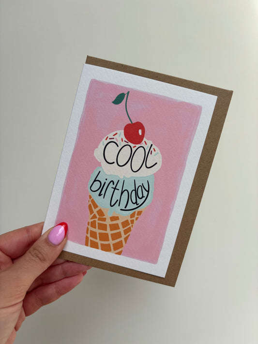 A6 premium textured recyclable greeting card with white border and pink background with an ice cream illustration with vanilla and mint scoops on a waffle cone, topped with sprinkles and a cherry and the handwritten words “cool birthday”. Brown Kraft envelope included.