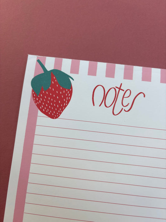 Pink and white striped notepad with a strawberry illustration on each corner. The notepad has the word ‘notes’ written in cursive at the top.