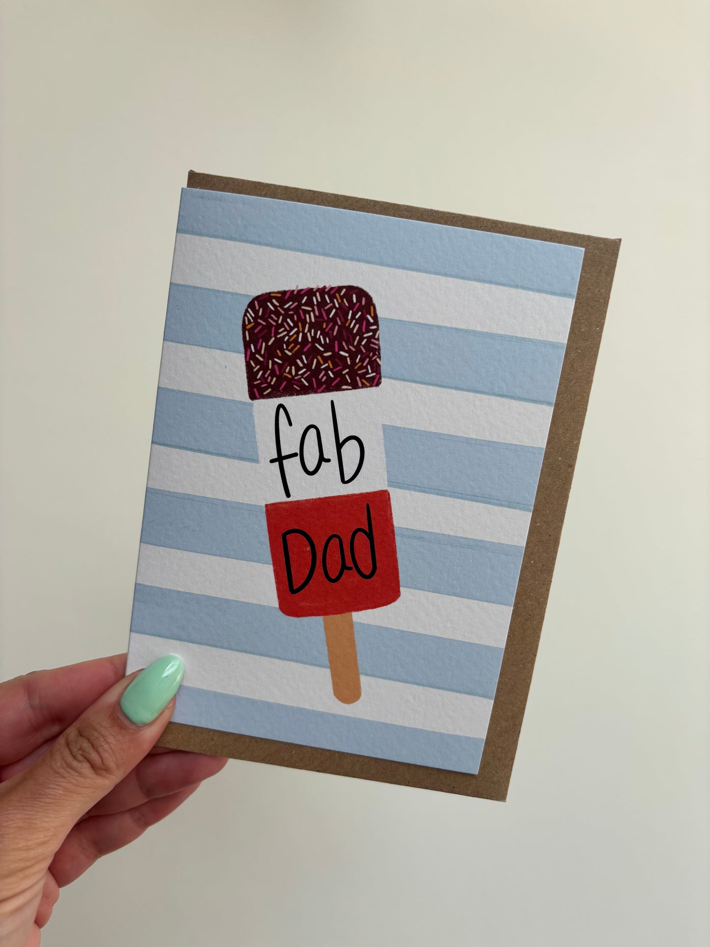 A6 card with blue and white horizontal stripes background featuring ice lolly and the word ‘fab dad’. Including brown Kraft envelope.