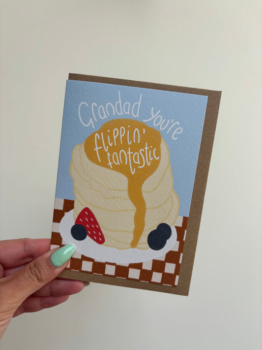 A6 premium textured greeting card with blue background, a stack of pancakes with drizzling syrup, berries and chequered brown tablecloth. Includes brown Kraft envelope.