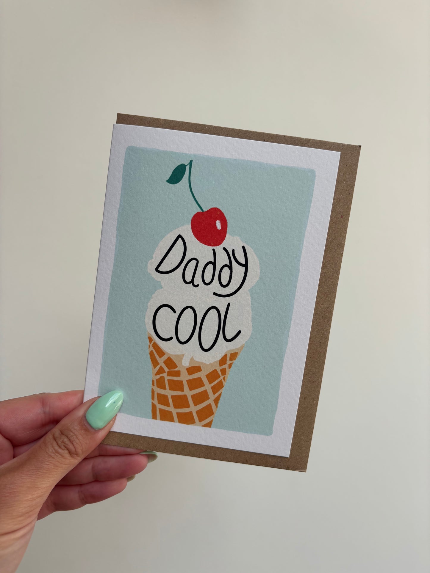 A6 white greeting card with mint green background featuring vanilla ice cream with cherry on top and wording ‘Daddy Cool’ . Features brown Kraft envelope.
