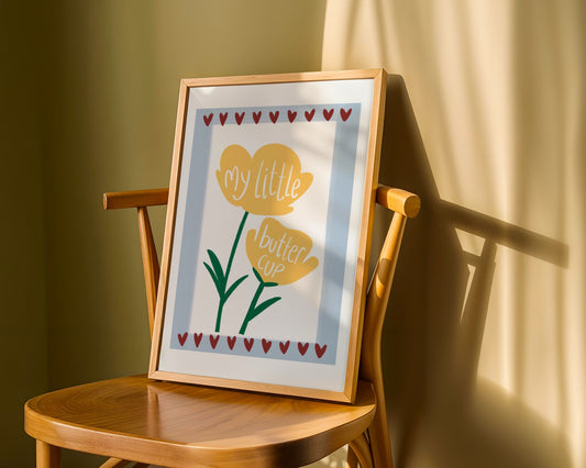 Kids wall print with white background,   light blue border and burgundy love hearts top and bottom with an illustration of two yellow buttercups and the words “my little buttercup”.
