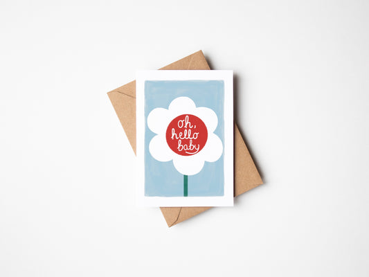 A6 premium textured recyclable card with white border, blue background and white daisy with red centre and the words ‘oh hello baby’ written inside centre of flower. Brown Kraft envelope included
