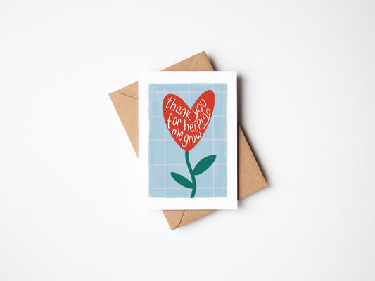 A6 premium textured recyclable teacher card with white border and blue and white grid background and red flower in a heart shape with the words “thank you for helping me grow” handwritten within it. Brown Kraft envelope included.