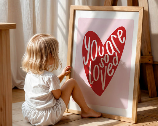 Kids wall art with white border, pink background, red heart and the words ‘you are so loved’ in white hand written text.
