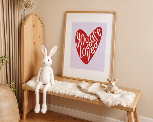 Kids wall art with white border, lilac background, red heart and the words ‘you are so loved’ in white hand written text.