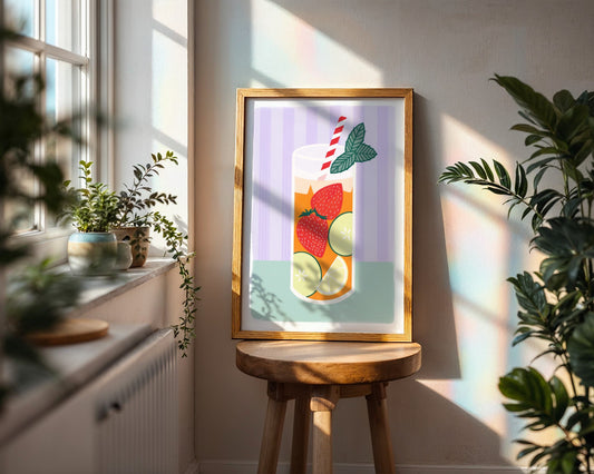 Framed artwork of a colourful Pimm’s drink with fruit on a kitchen counter with a bowl of lemons, a plant, and a cup.