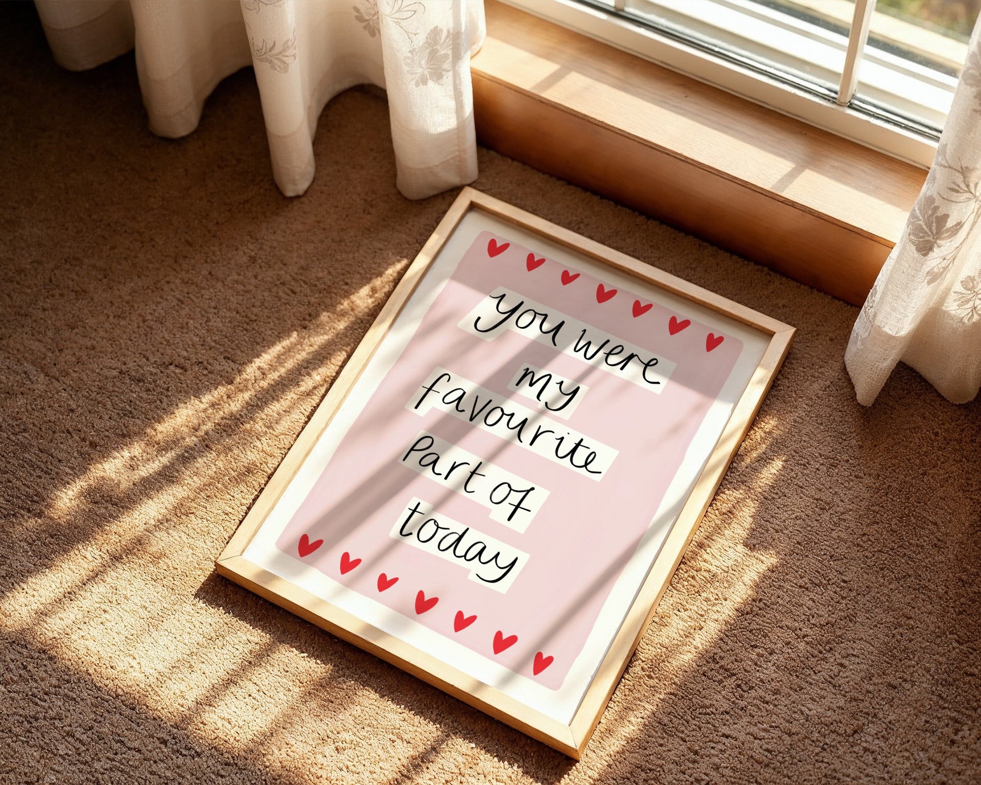 Framed quote on a pink background with red hearts, placed on a carpeted floor.