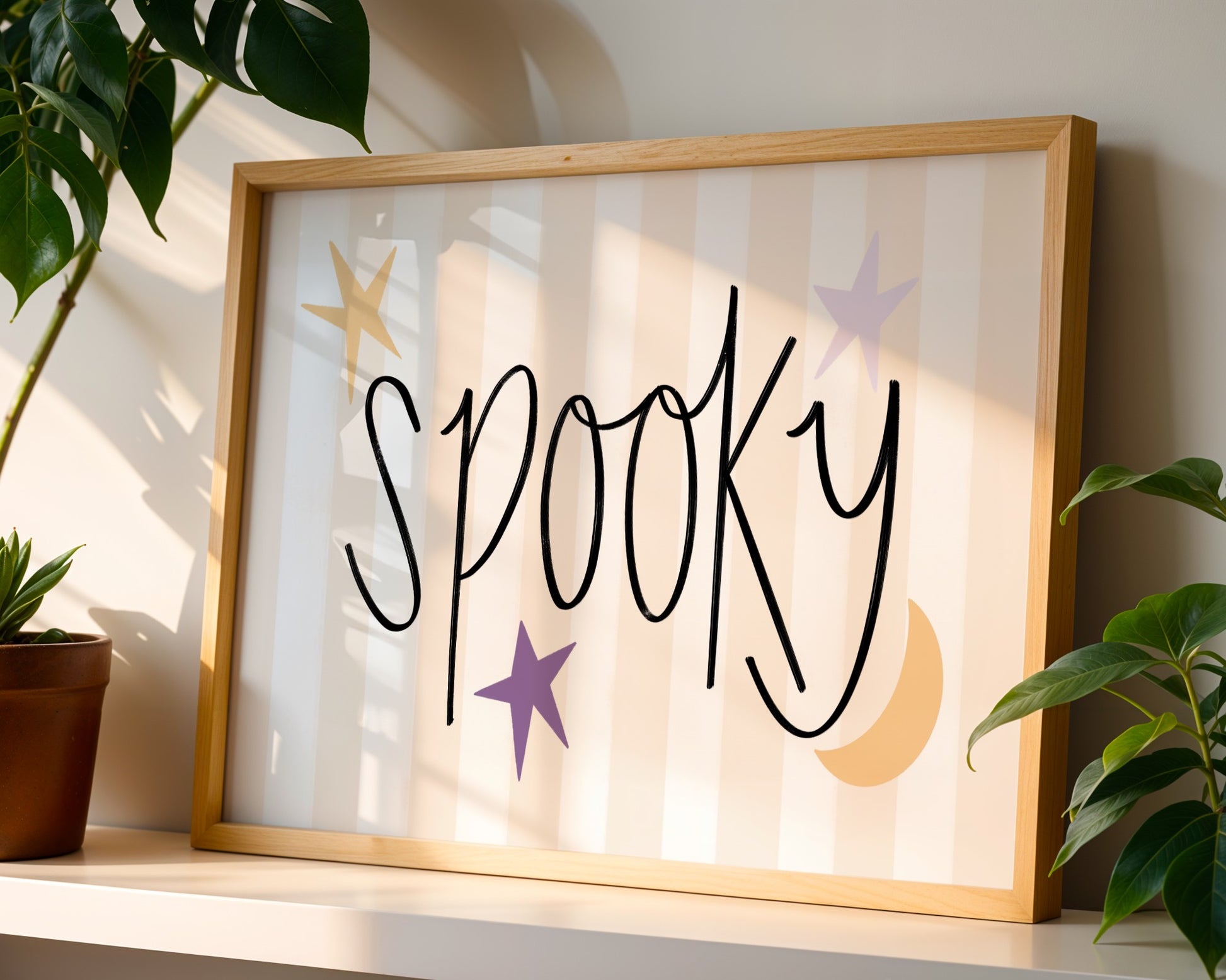 Framed artwork with the word 'Spooky' on a shelf with plants.