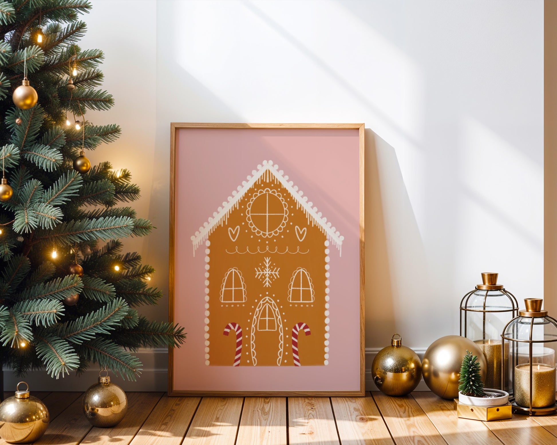 Framed artwork of a gingerbread house on a wall next to a decorated Christmas tree.