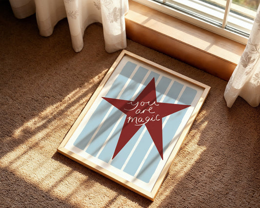 Framed artwork with a red star and 'You are magic' text on a carpeted floor.
