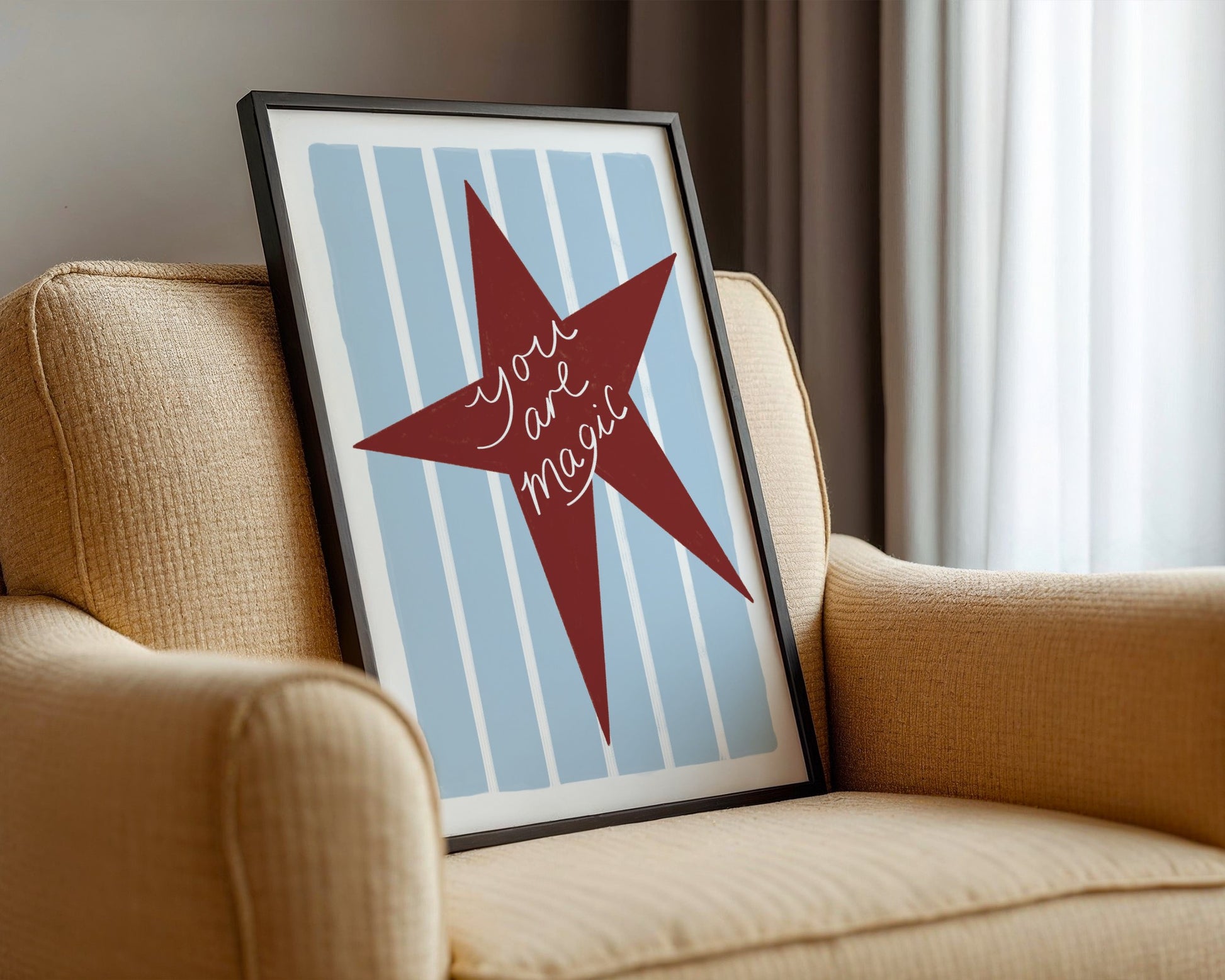 Framed artwork with a red star and text on a blue striped background, placed on a beige armchair.