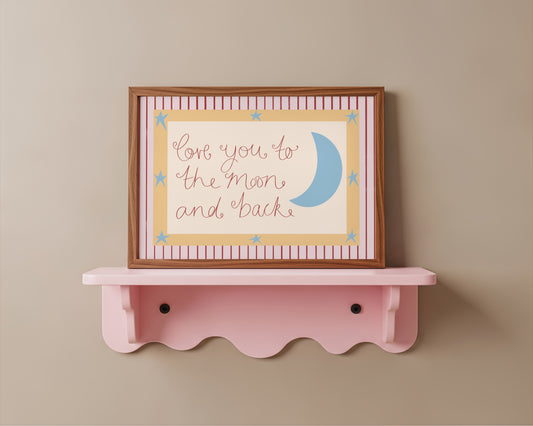 Framed artwork with 'Love you to the moon and back' text on a pink shelf against a beige wall.