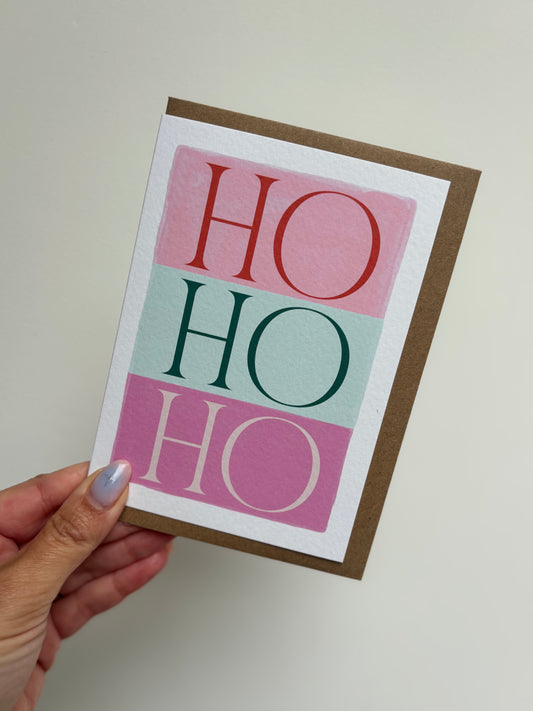 Card with 'HO HO HO' text held by a hand against a plain background