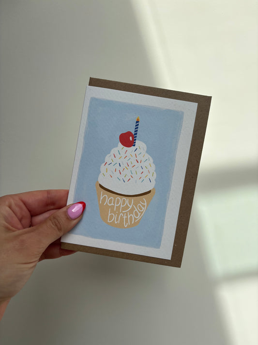 A6 premium textured recyclable greeting card with white border and blue background with white icing cupcake design featuring colourful sprinkles, blue and white striped candle and cherry on top. Brown Kraft envelope included. 