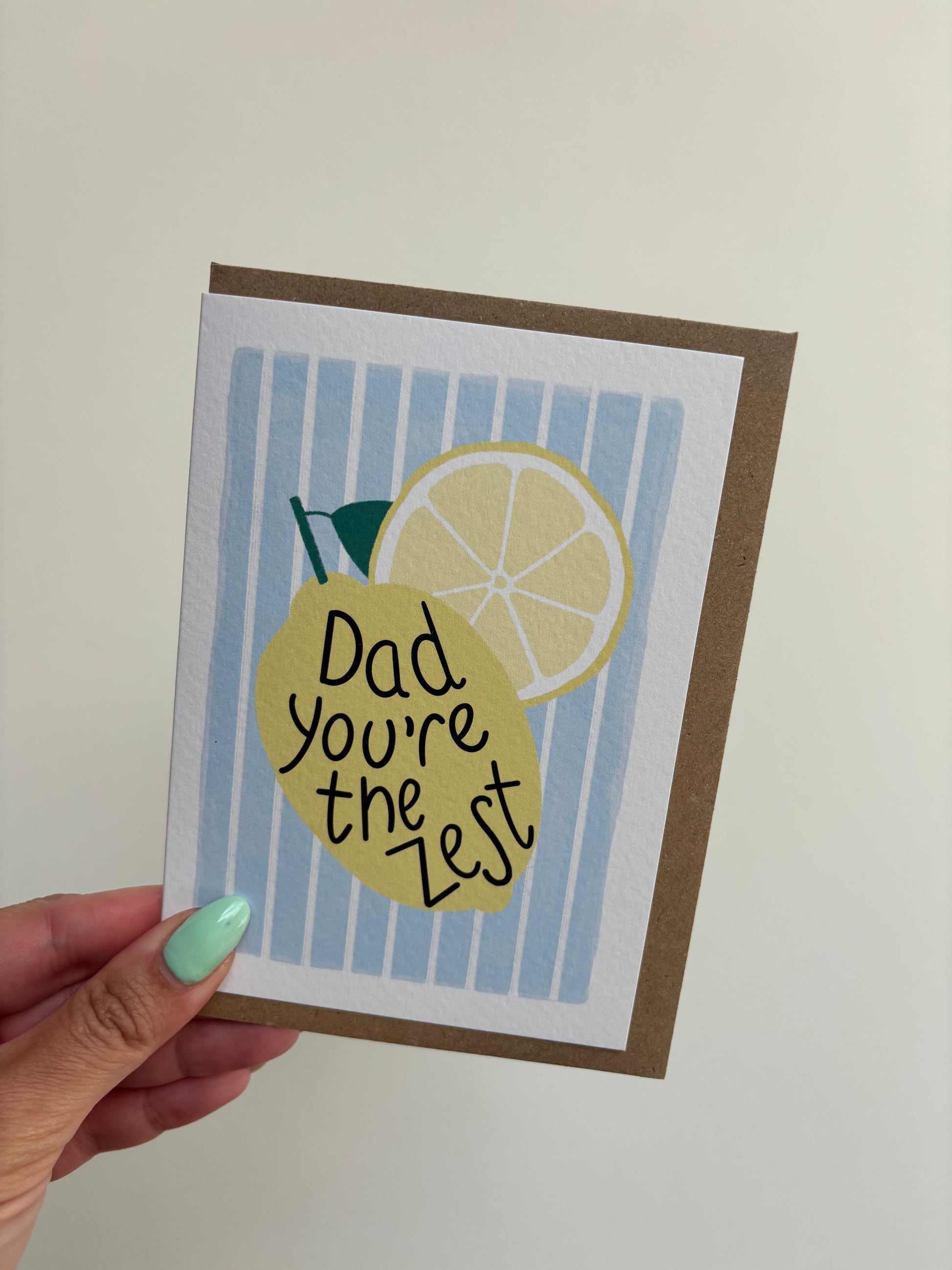 A6 white greeting card with blue and white striped background featuring a lemon and wording ‘Dad, you’re the zest’ . Features brown Kraft envelope.
